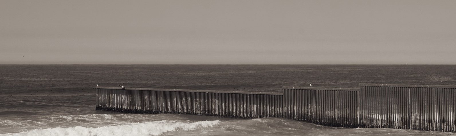 A fence running out into the ocean, with a wave in the foreground